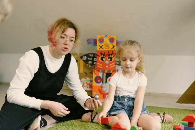 Toddler building with wooden blocks alongside a teacher